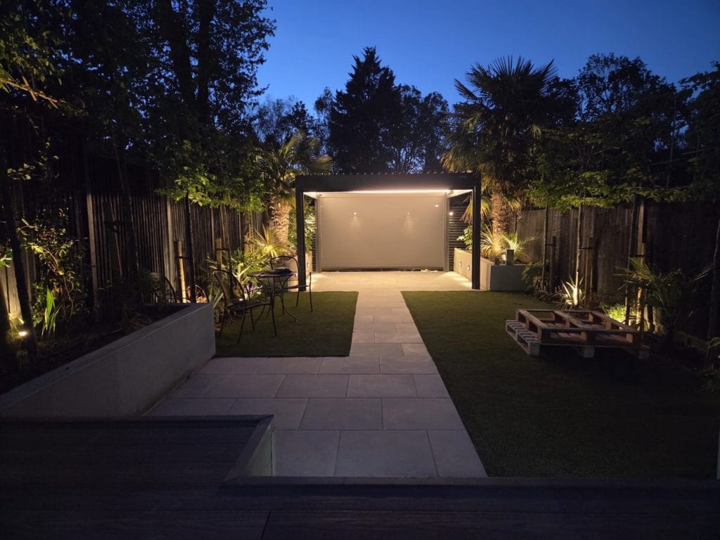 Contemporary garden at dusk with lighting, a modern garden room and slatted screens, by Flourish Landscaping