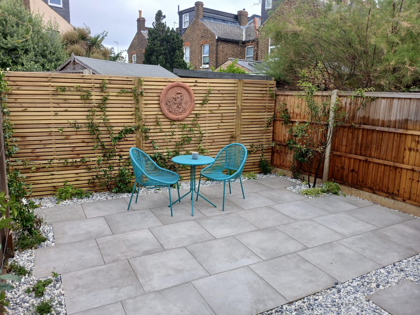 Courtyard garden with porcelain paving and a blue bistro set, by Flourish Landscaping