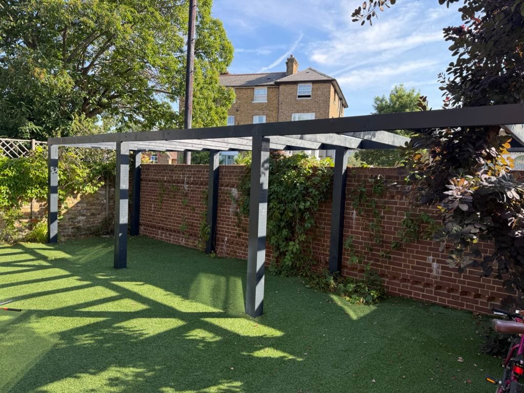 Metal slatted pergola, artificial lawn and exotic planting in a New Malden garden, by Flourish Landscaping