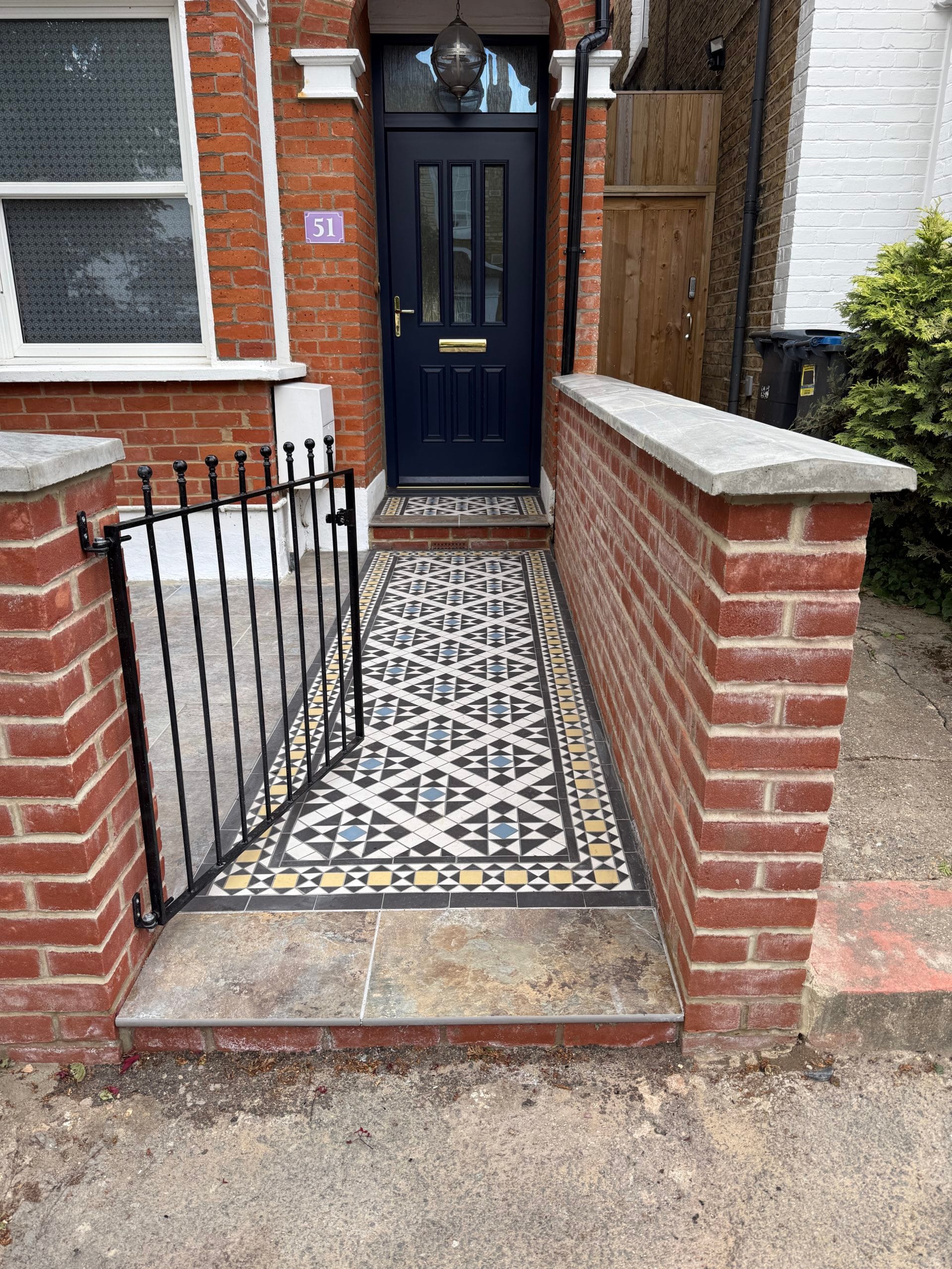 Restored Victorian encaustic tiled front path in black, white and grey leading to a navy front door, with reinstated brick walls and wrought-iron railings on a period property in Norbiton, Kingston upon Thames, by Flourish Landscaping